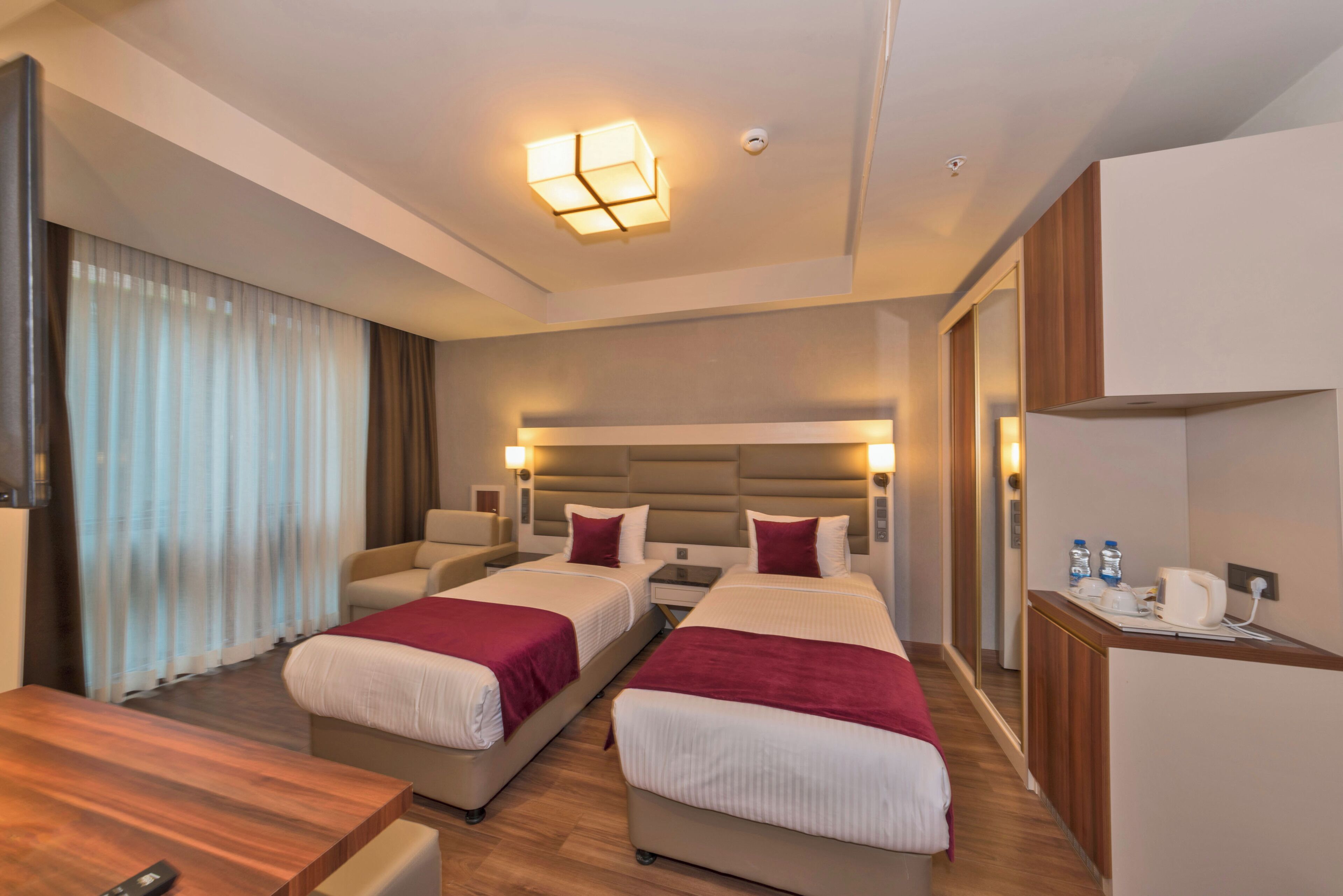 A hotel room with two beds, a desk, a chair, a nightstand, and a mirror.