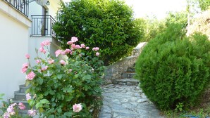 Un sendero de piedra bordeado de abundante vegetación y rosas rosadas que conduce a una escalera de piedra.
