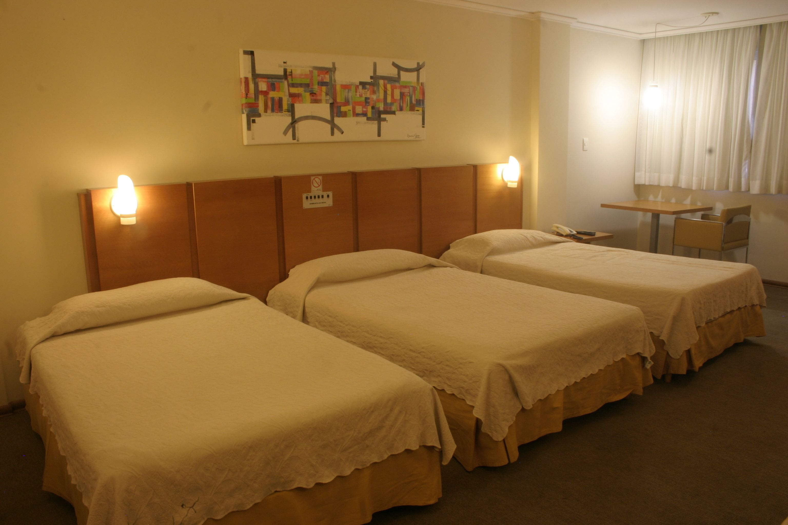 Een hotelkamer met drie eenpersoonsbedden, een klein tafeltje en een stoel.