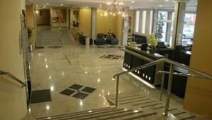 Un hall de hotel con una escalera, zona de estar, mostrador de recepción y un candelabro.