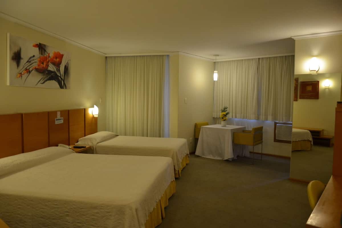 Ein Hotelzimmer mit zwei Betten, einem kleinen Tisch mit einer Vase, einem Sessel, einem Schreibtisch und einem Spiegel.