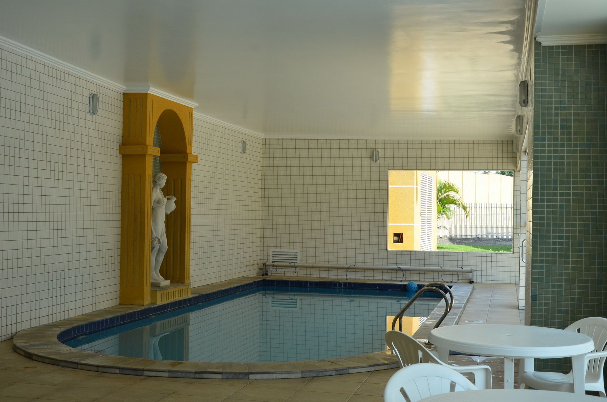 A swimming pool area with tiled walls, a statue, and a view of a palm tree outside.