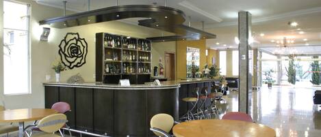Zona de bar con una barra curva, diversas opciones de asientos que incluyen mesas redondas y sillas, y un elemento decorativo en la pared.