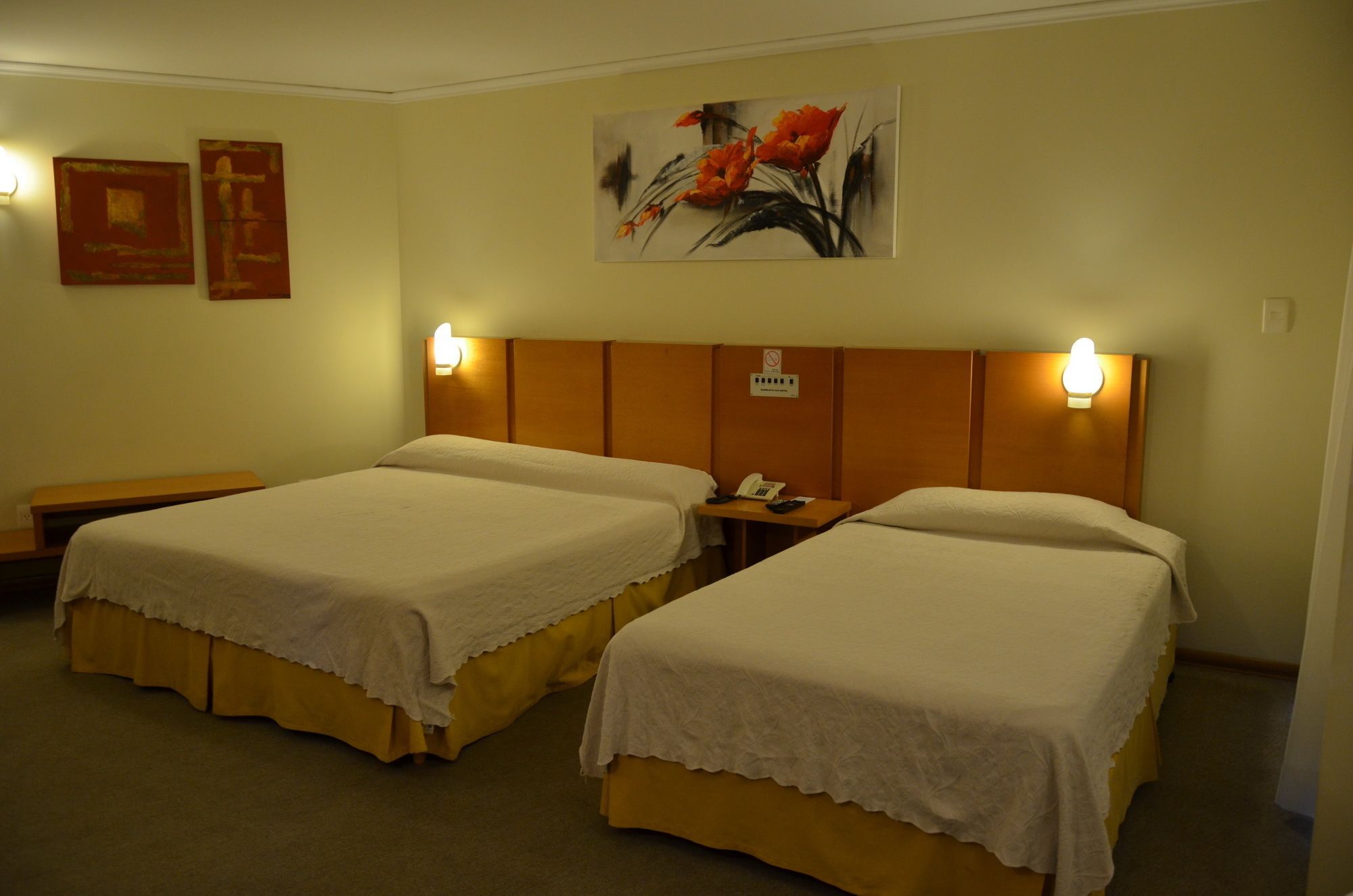 A hotel room with two beds, a nightstand, a wall-mounted telephone, and two paintings.
