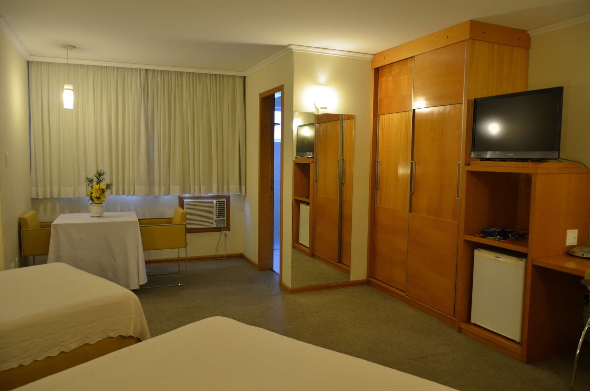 Habitación de hotel con dos camas, una mesita con un florero, televisión, minibar y armario.
