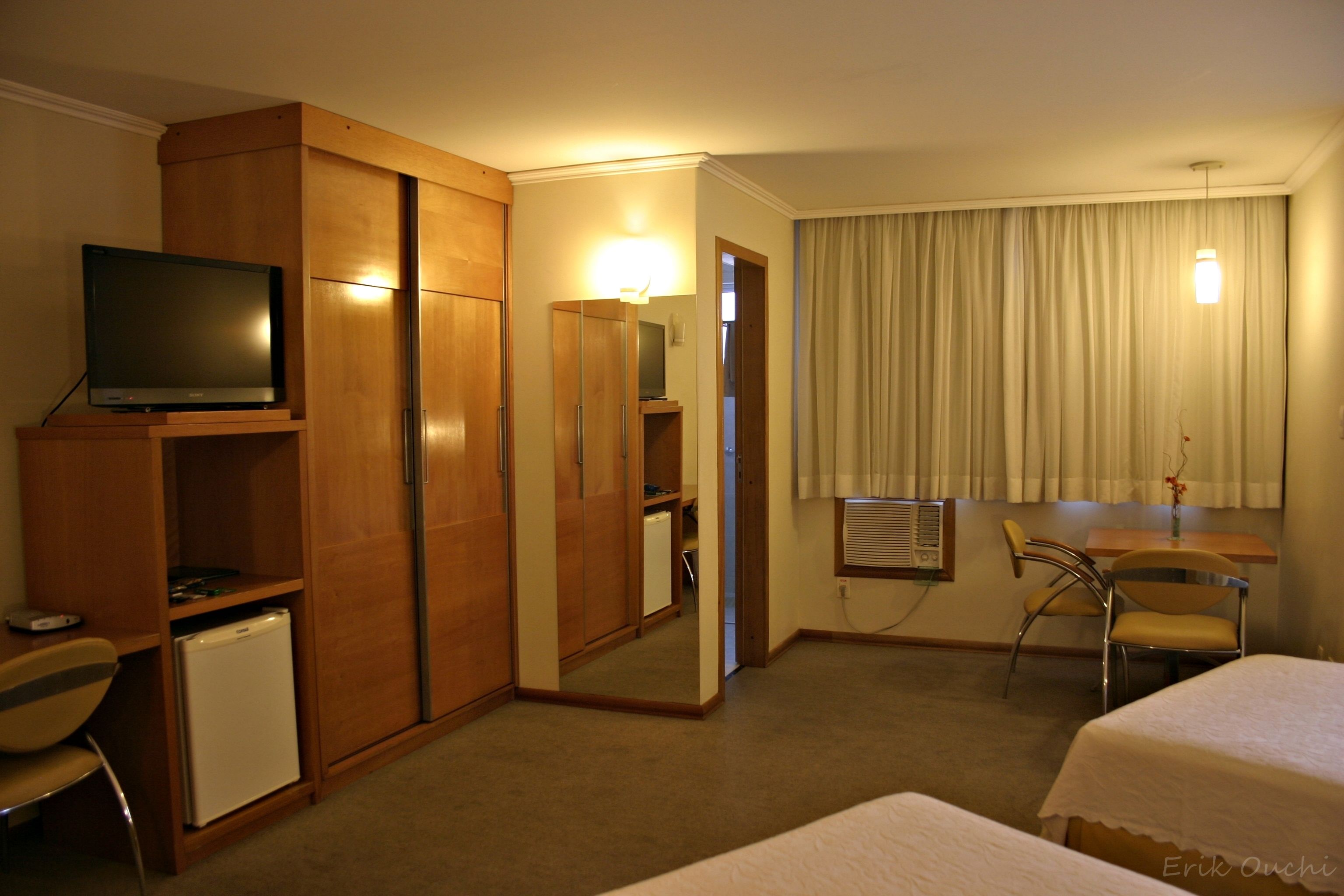 A hotel room with a bed, a desk, a chair, a television, a wardrobe, and a mirror.