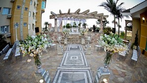 Montaje para una boda al aire libre con piso de piedra, arreglos florales blancos y una estructura de pérgola.