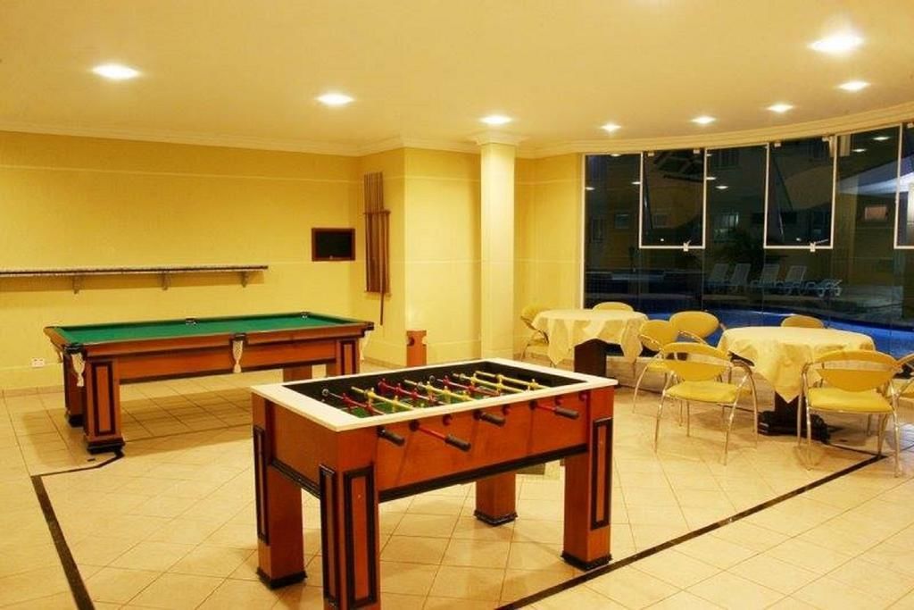 Una habitación con mesa de futbolín, mesa de billar y varias mesas con sillas.