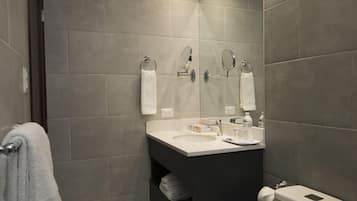 A modern bathroom with grey tiles, a white toilet, a sink with a mirror, and a towel rack.