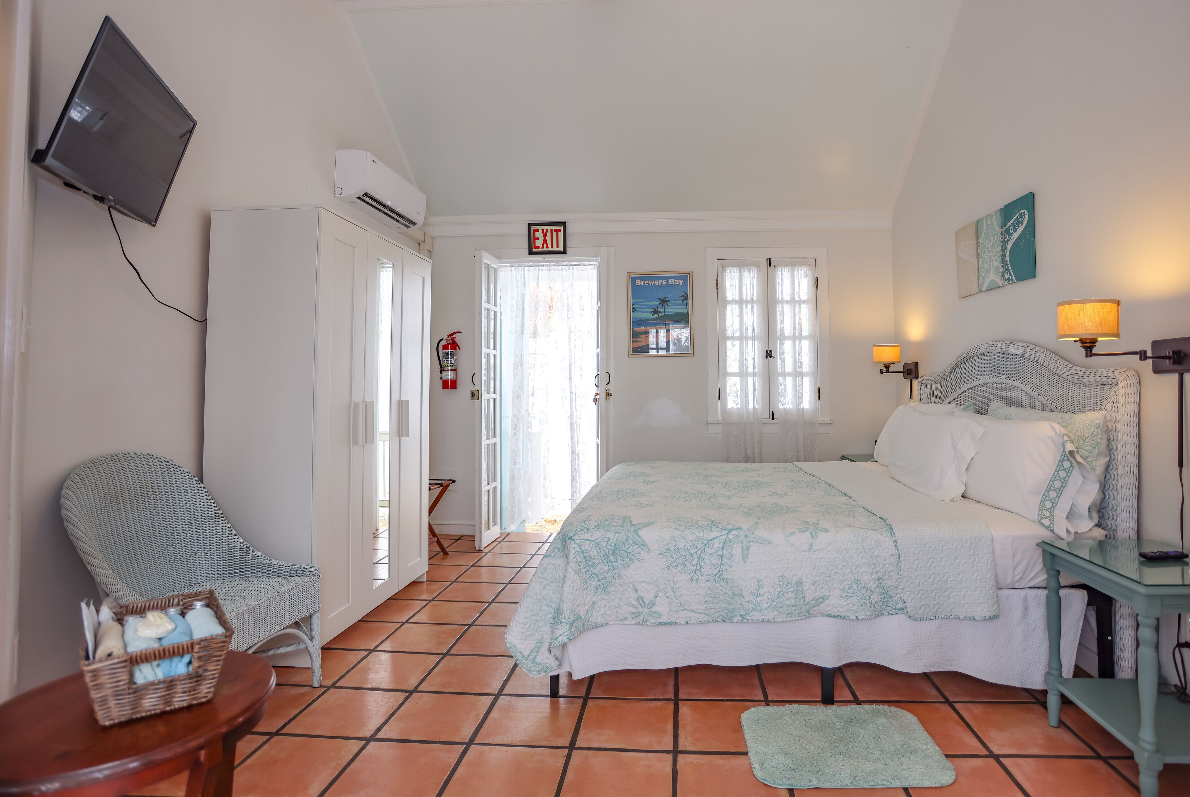 A bedroom with a bed, a chair, a TV, and an exit sign.