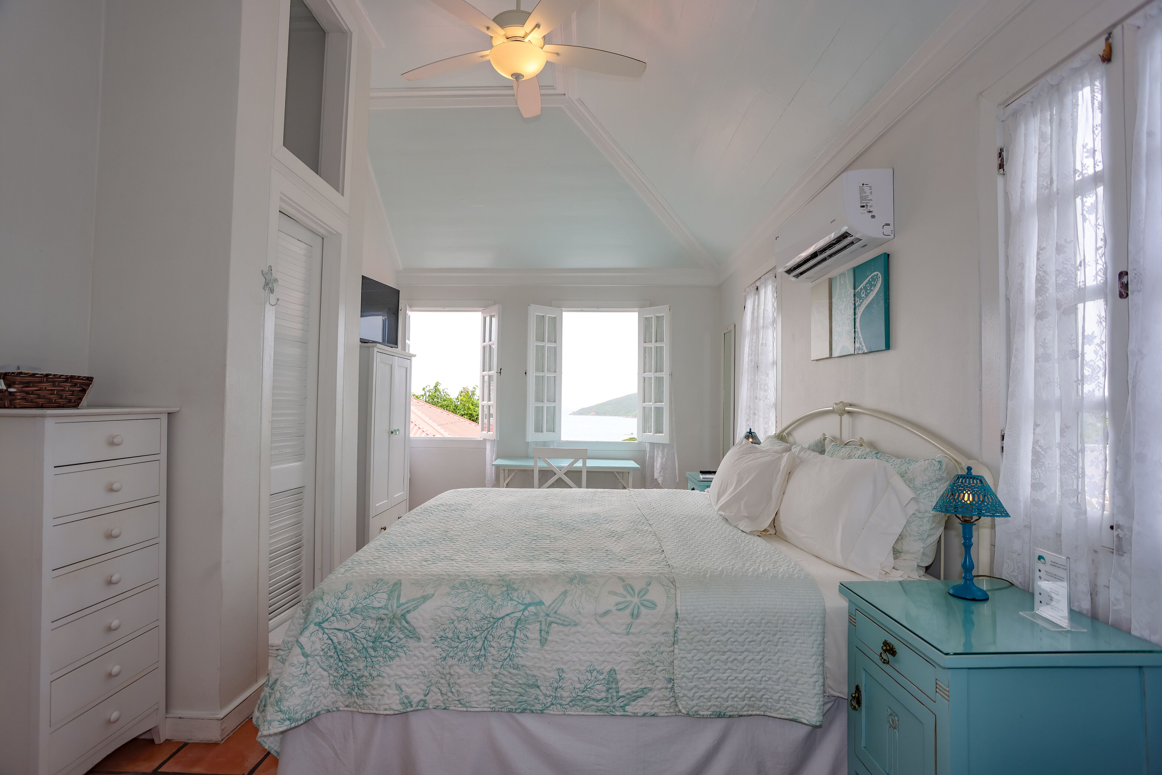 Une chambre à coucher comprenant un lit, une commode, une table de chevet et un ventilateur de plafond.
