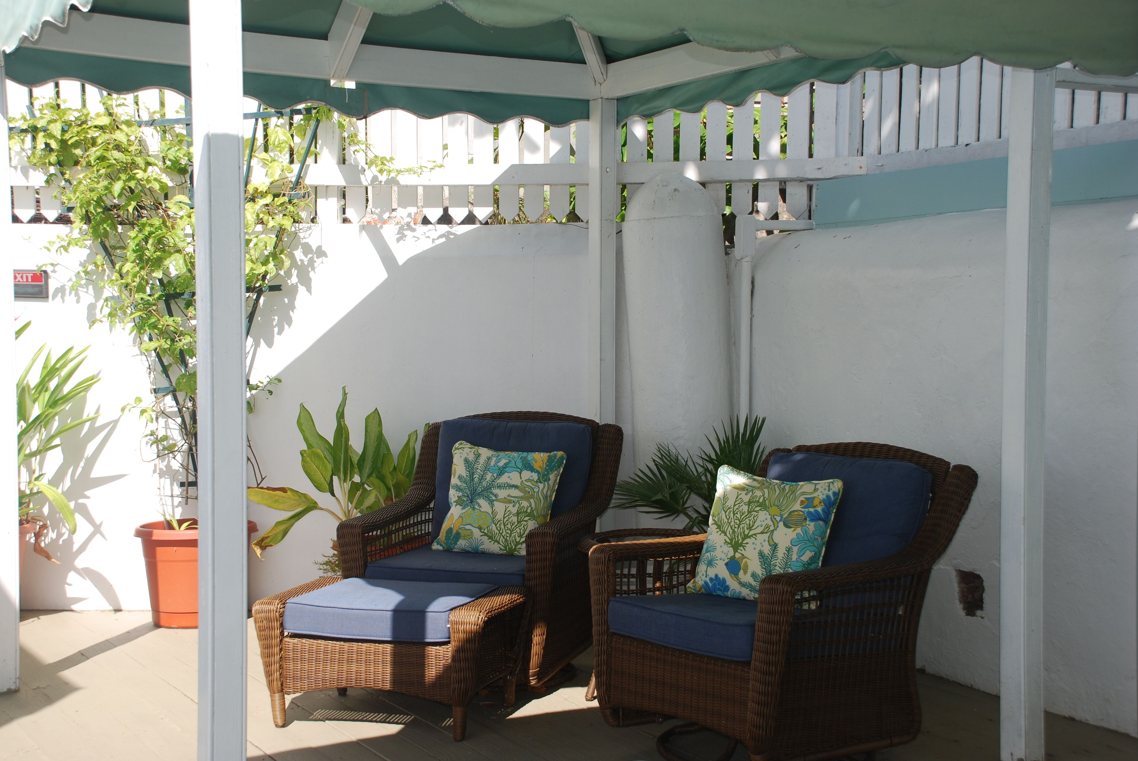 Two wicker chairs with blue cushions under a white pergola with a green awning.