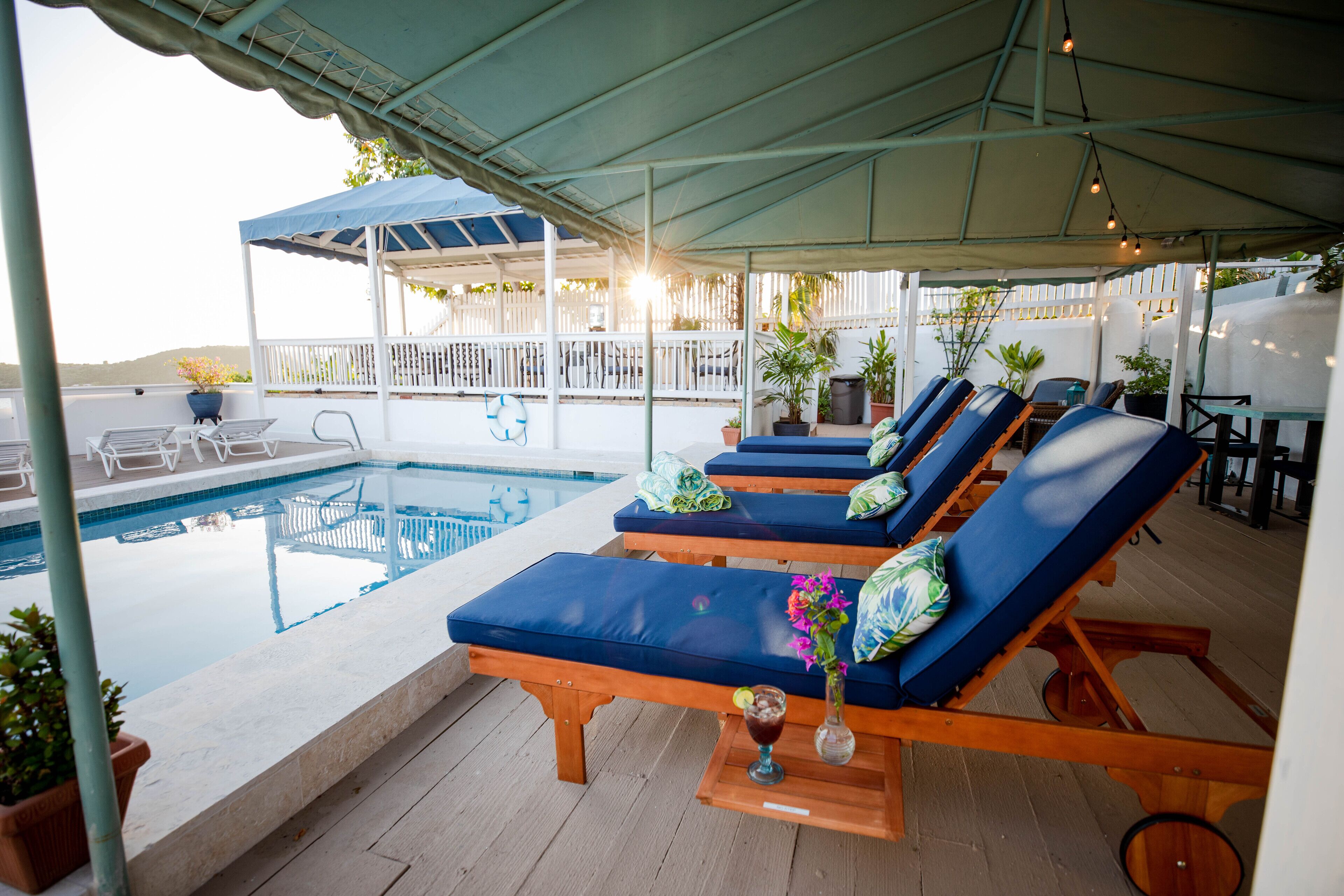 A poolside area with lounge chairs, a covered seating area, and a view of the pool.