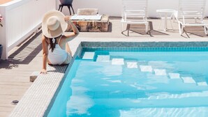 A pool area with a view of the sea, lounge chairs, and a person sitting by the pool. - At Home in the Tropics (St. Thomas)