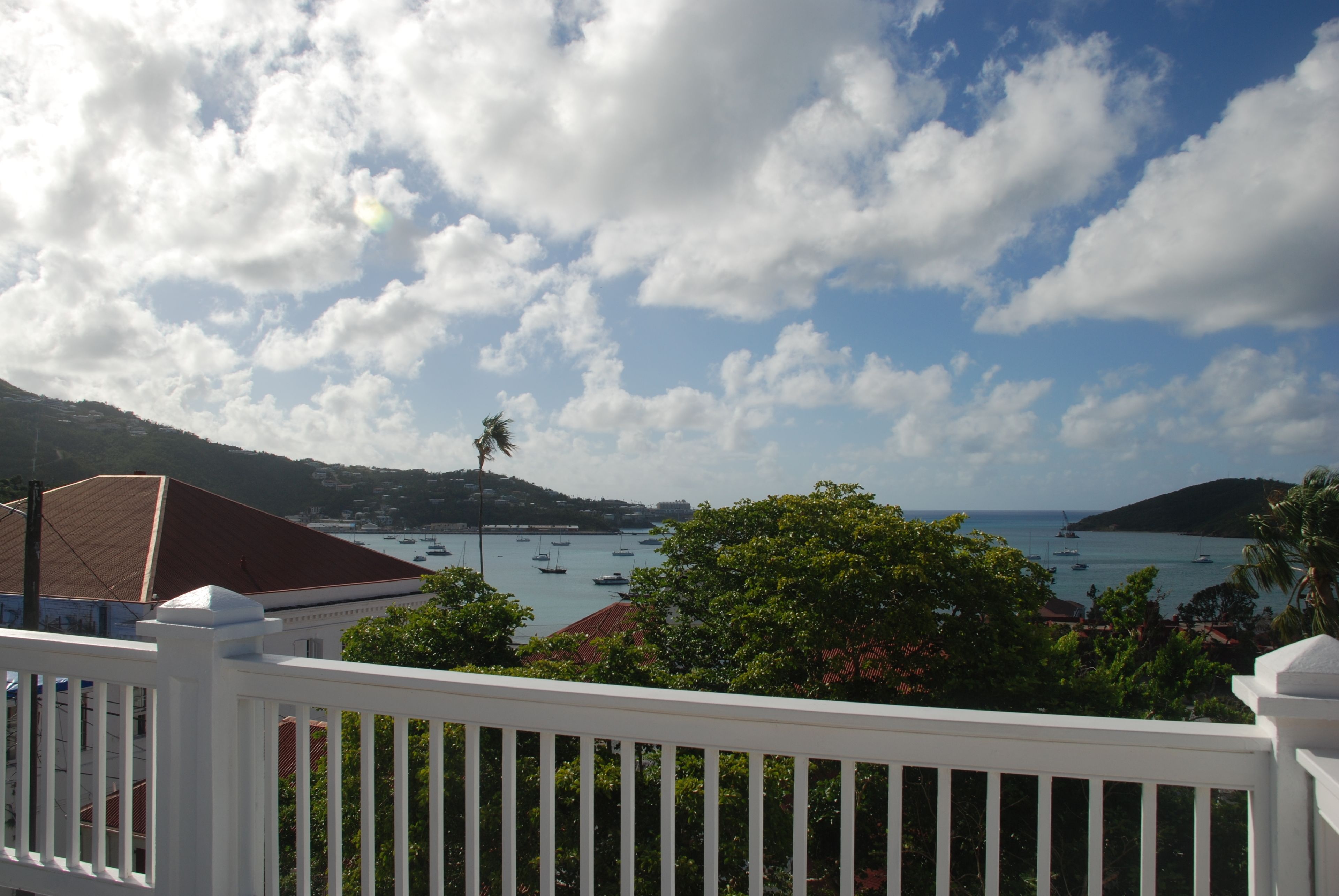 A coastal view with boats, a white railing, and lush greenery.