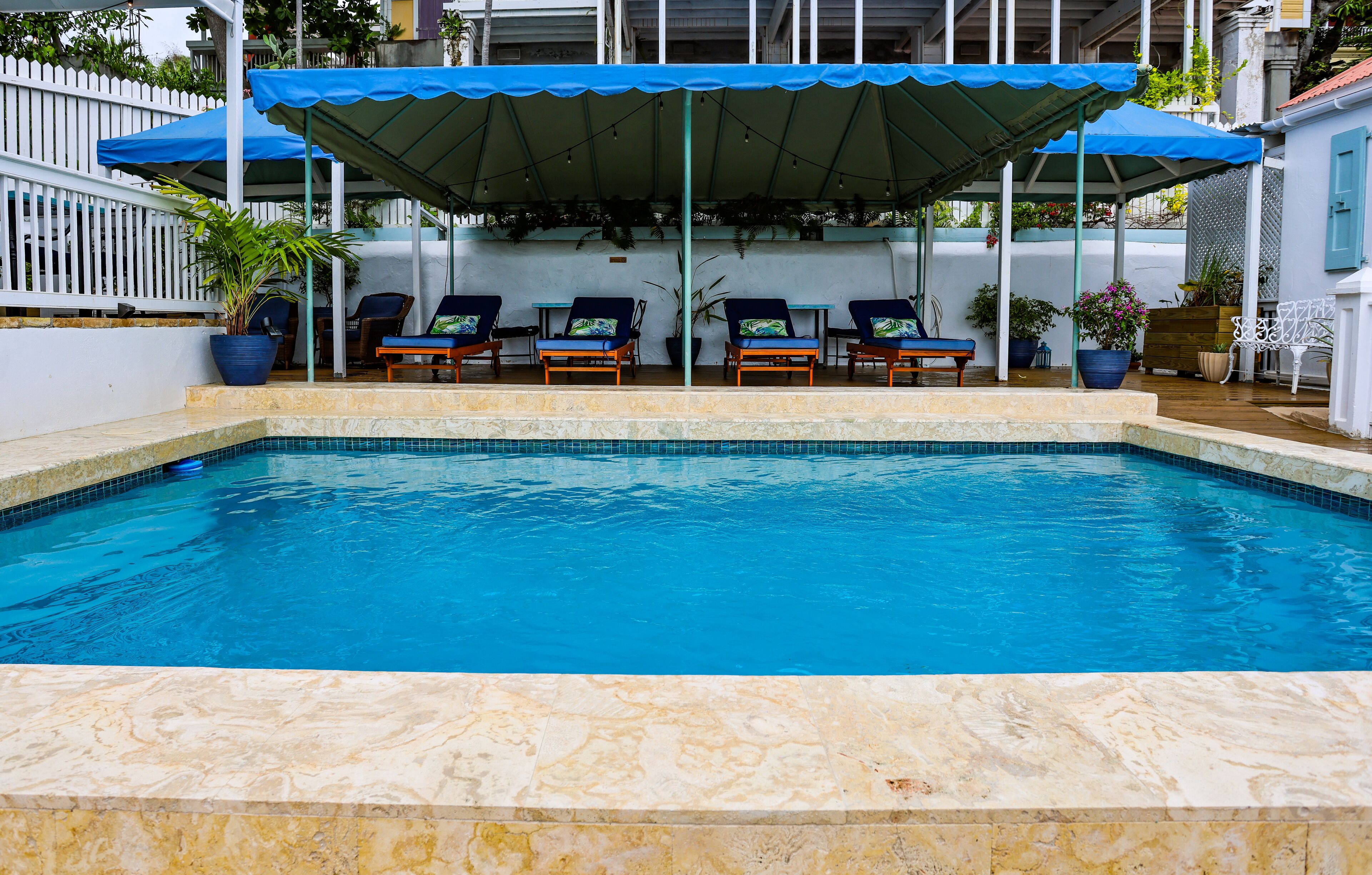 A swimming pool with a covered seating area and lounge chairs.