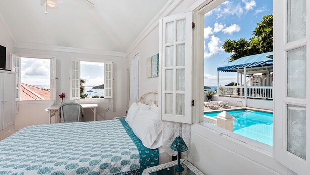 A bedroom with a large bed, a desk, and a view of a swimming pool. - At Home in the Tropics (St. Thomas)