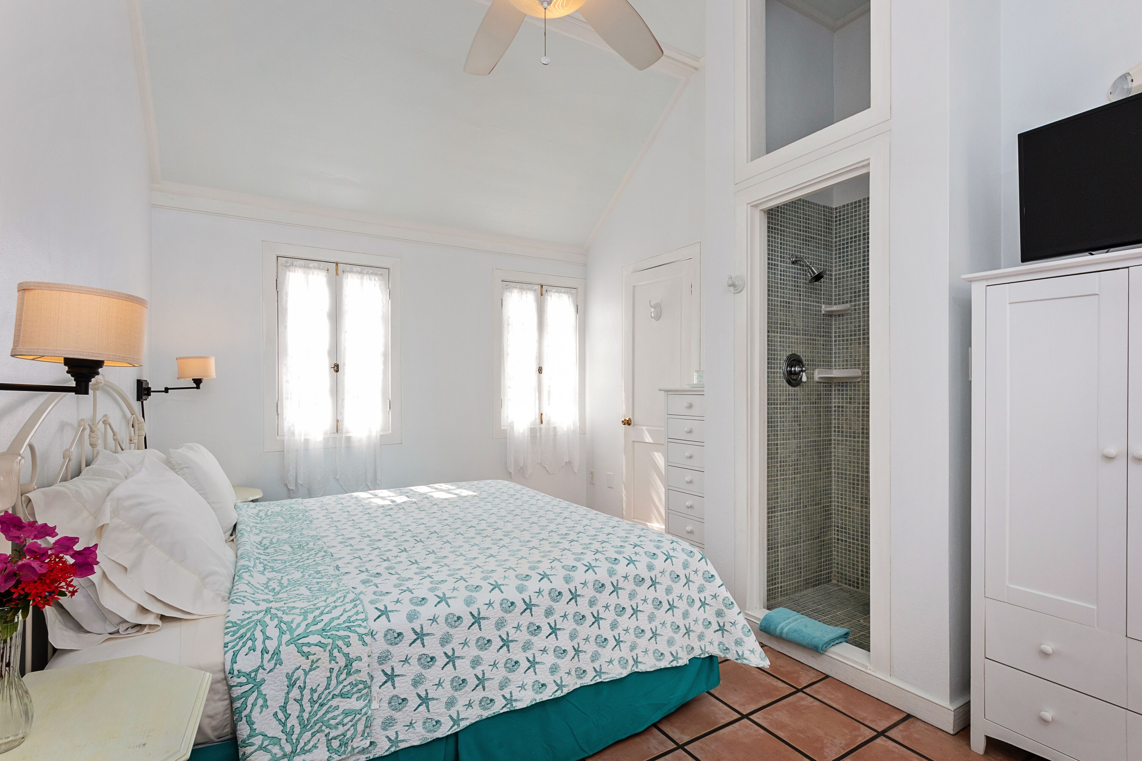 Une chambre à coucher comprenant un lit, une table de chevet, une lampe, une fenêtre et un espace douche.