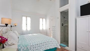 Une chambre à coucher comprenant un lit, une table de chevet, une lampe, une fenêtre et un espace douche.