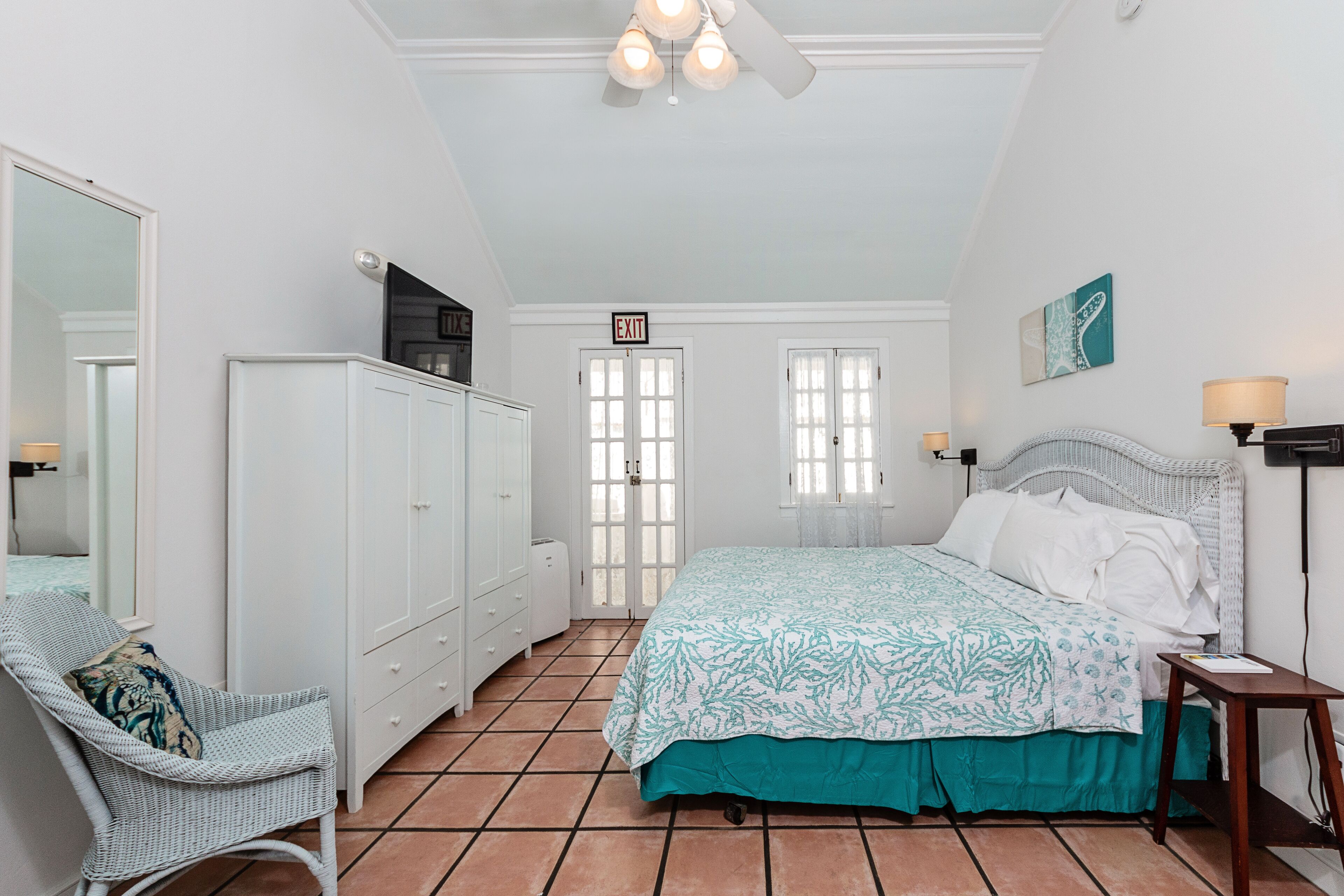 A bedroom with a bed, a dresser, a chair, and an exit sign.