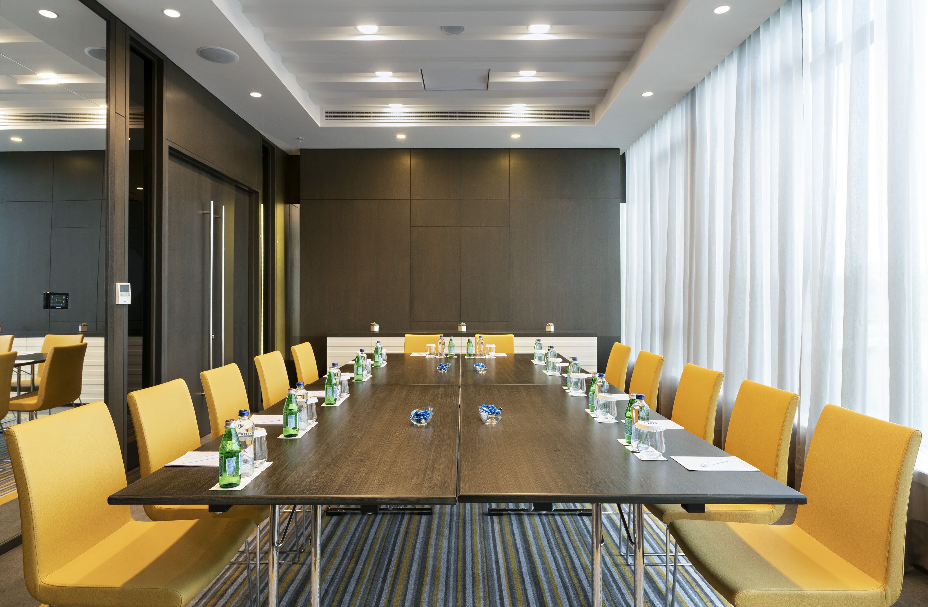 A conference room with a long table, yellow chairs, and water bottles.