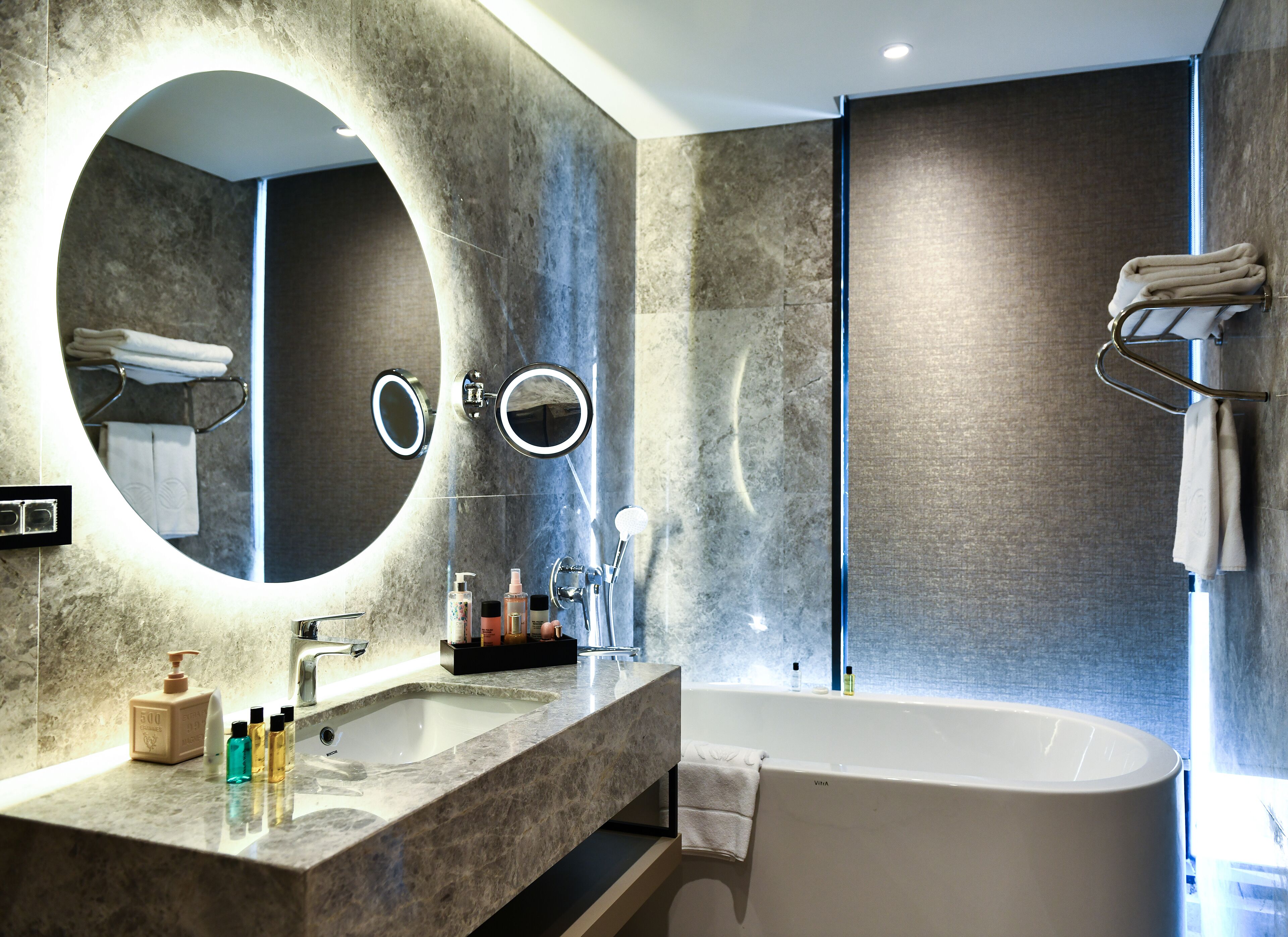 A modern bathroom with a large mirror, a bathtub, and a vanity with toiletries.