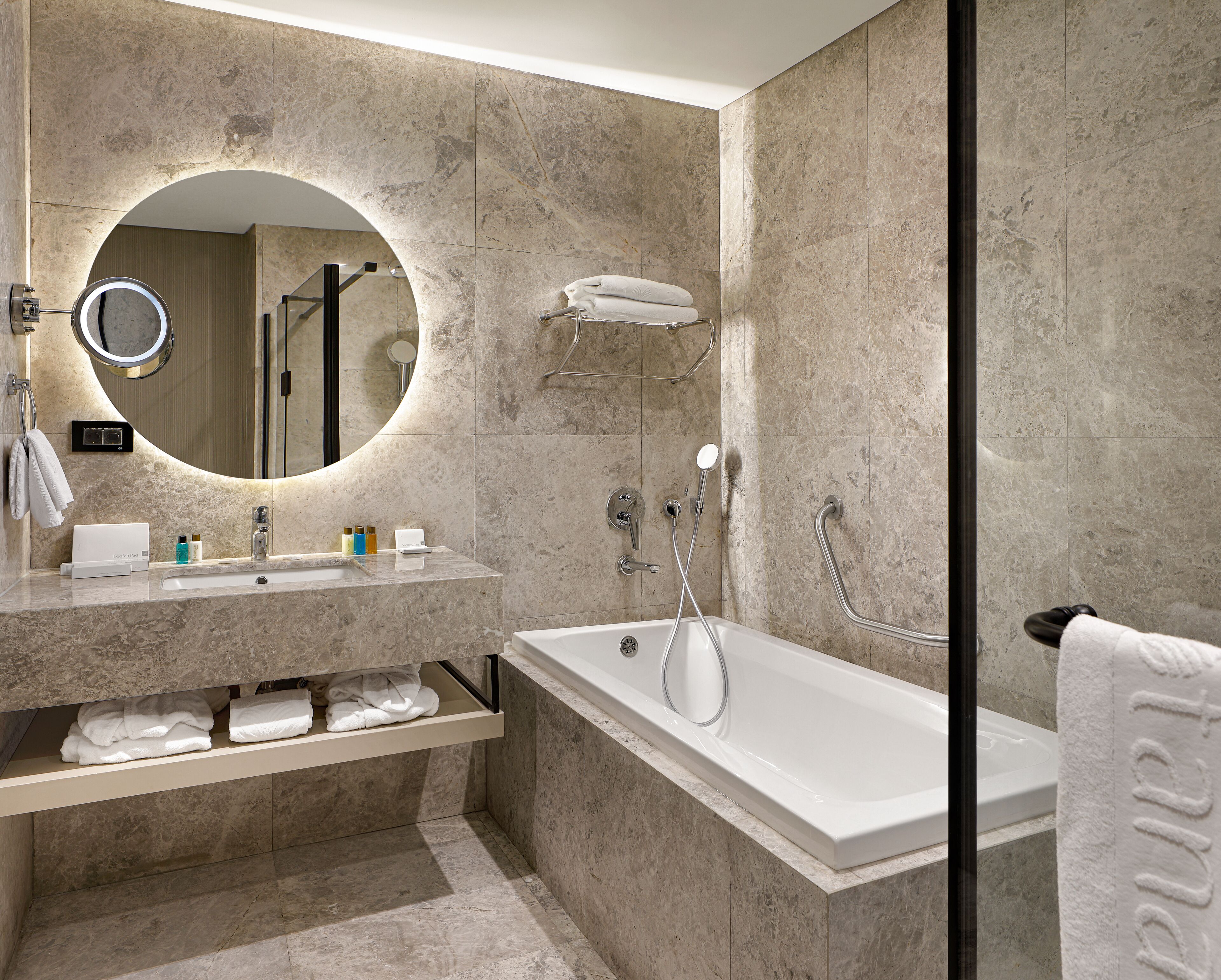 Un baño moderno con lavamanos de mármol, un espejo grande, una bañera y un perchero para toallas.
