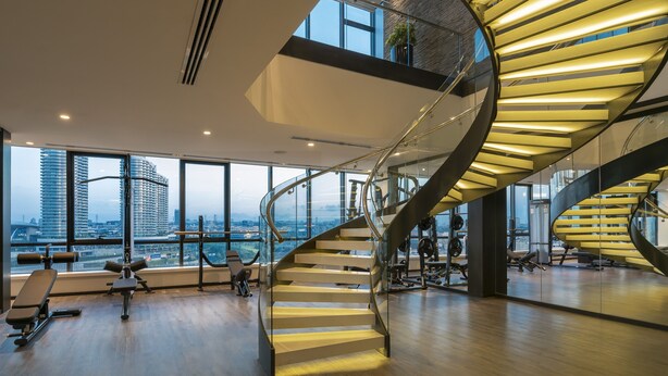 A modern gym with a spiral staircase, large windows, and exercise equipment. - Westside Residences By Rotana (Istanbul)