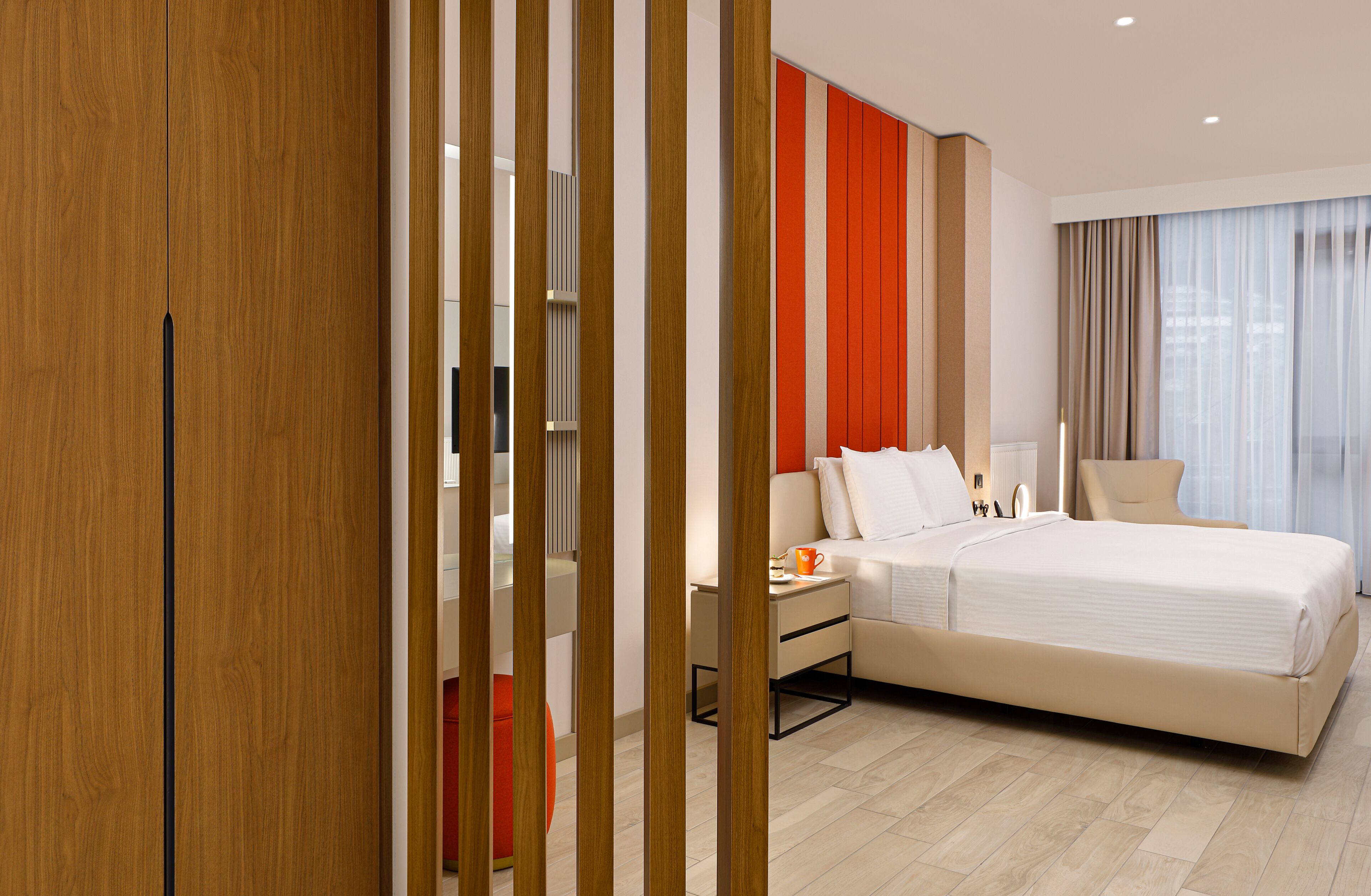 A modern hotel room with a large bed, a bedside table, a chair, and a view of the city through the window.