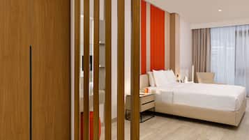A modern hotel room with a large bed, a bedside table, a chair, and a view of the city through the window.