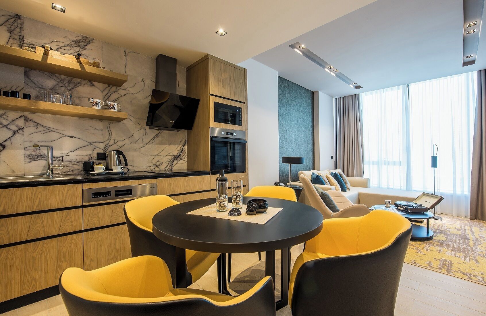 A modern hotel room with a kitchen area, dining space, and a living area with a sofa and a coffee table.