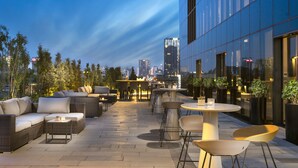 An outdoor seating area with wicker furniture and a glass table, overlooking a cityscape at dusk. - Westside Residences By Rotana (Istanbul)