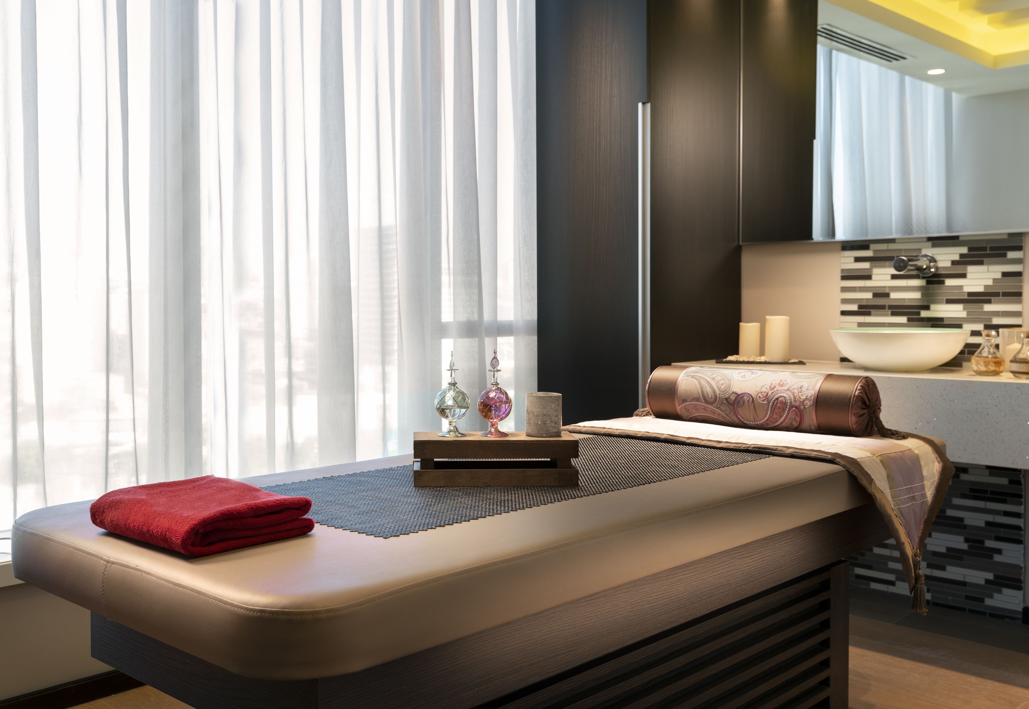 A modern spa room with a massage table, a red towel, and a small table with decorative items.