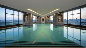 A large indoor swimming pool with a city view, stone walls, and a modern design. - Westside Residences By Rotana (Istanbul)