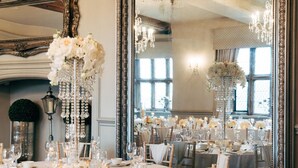 A formal dining room with ornate chandeliers, mirrored walls, and elegant table settings. - Weston Hall (Stafford)