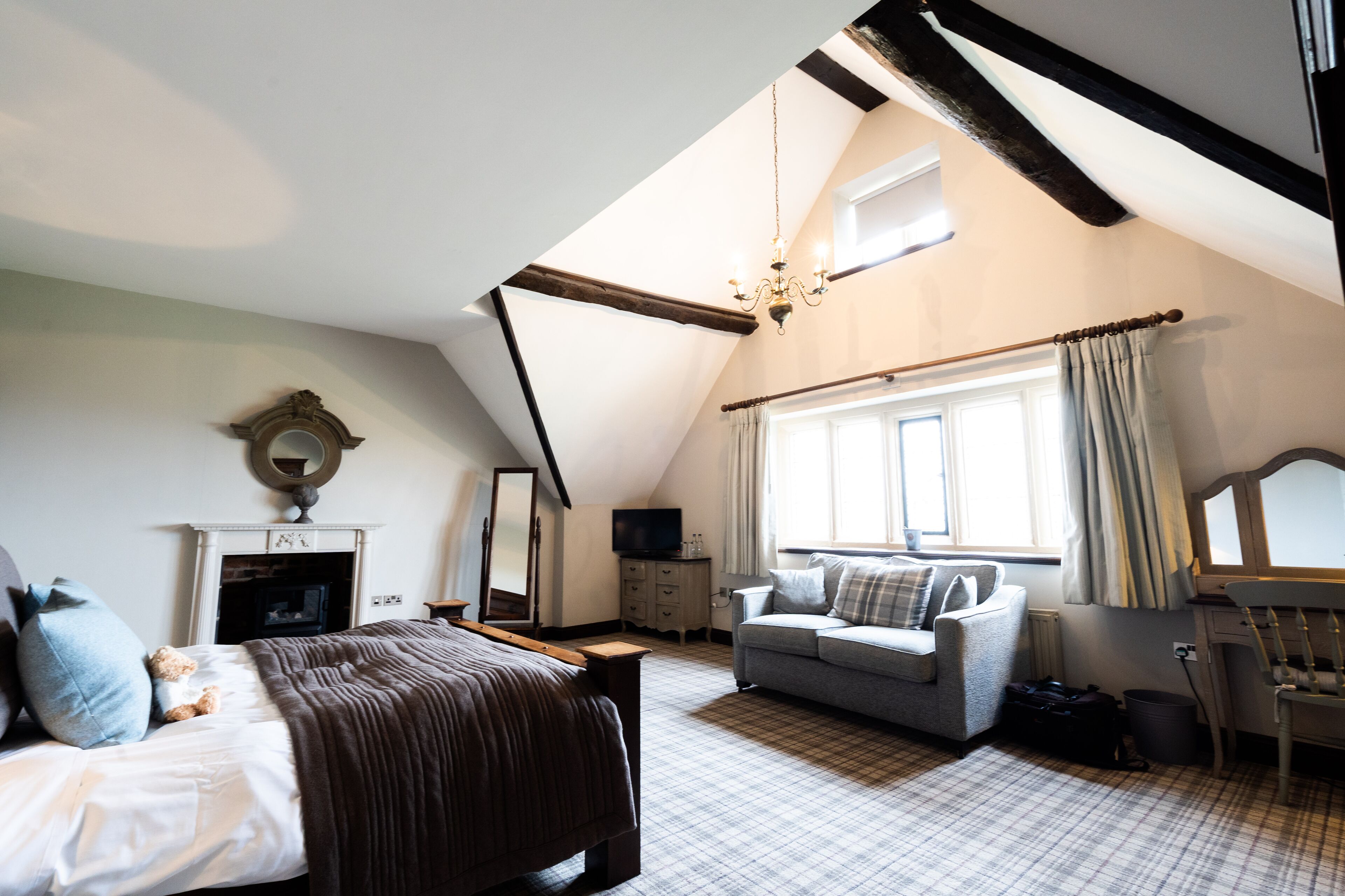 Ein Schlafzimmer mit Bett, Sofa, Fernseher, Kamin und einem Fenster mit Vorhängen.