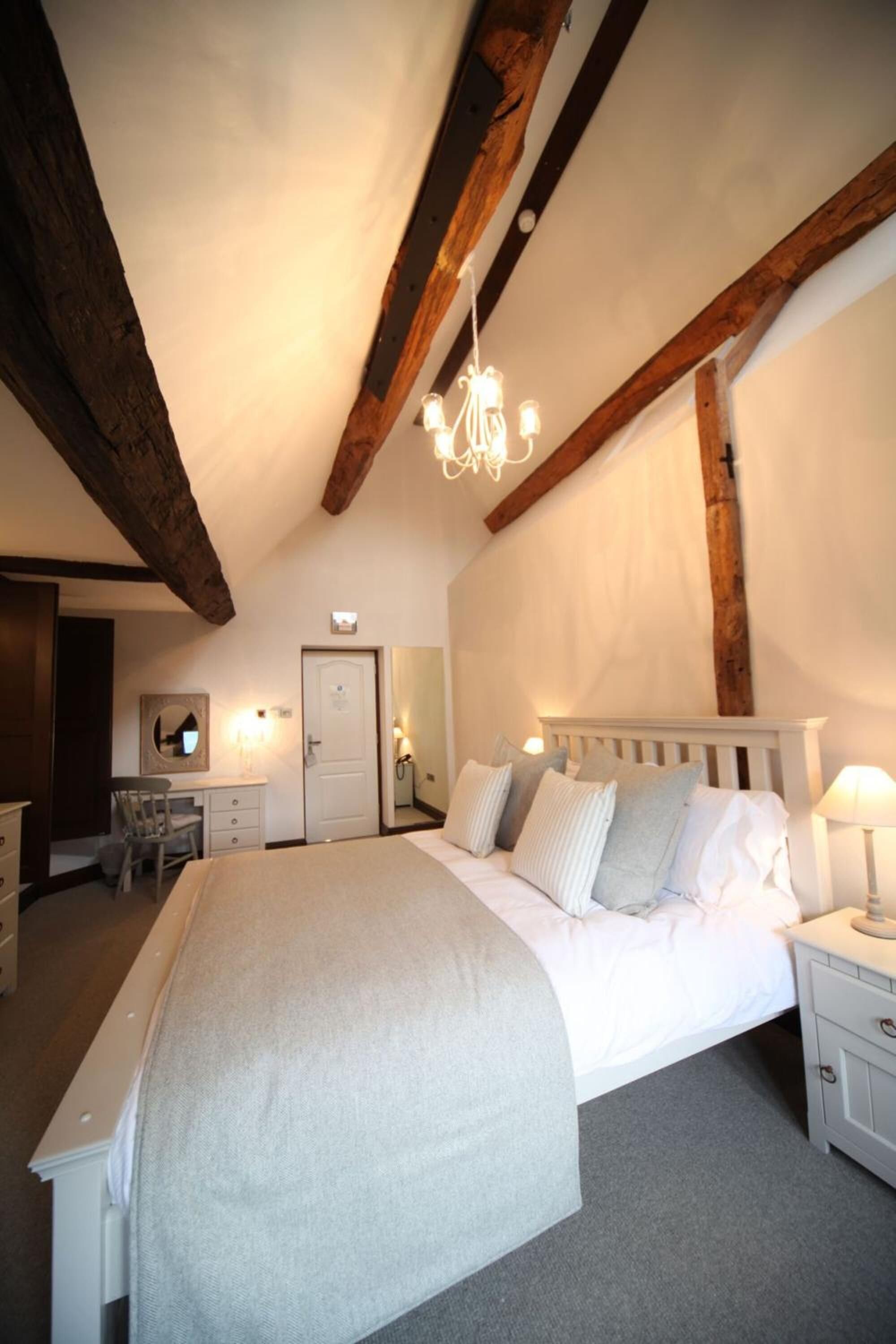 A bedroom with a large bed, wooden beams, a desk, and a chair.