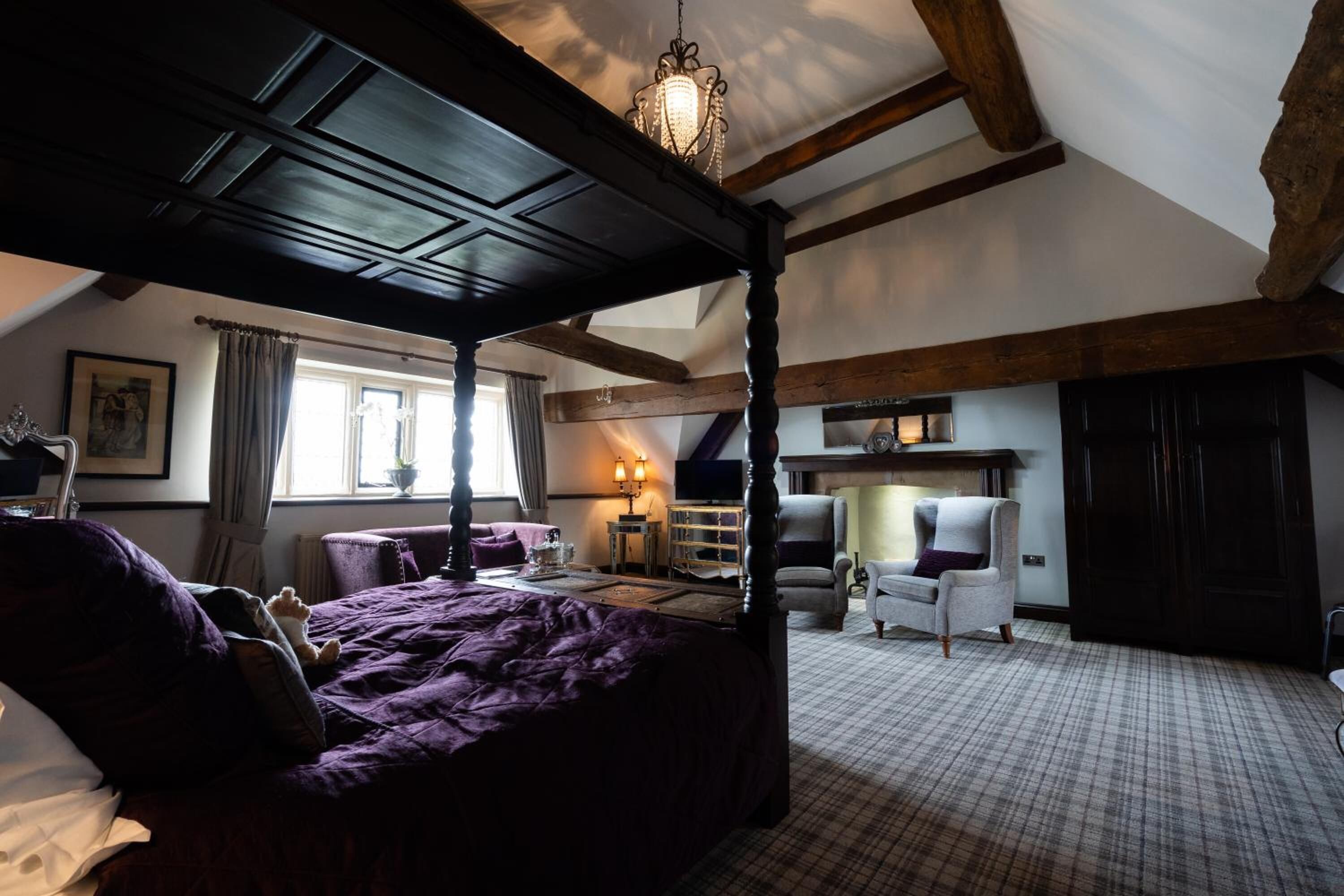 A bedroom with a four-poster bed, a chandelier, a television, and a fireplace.