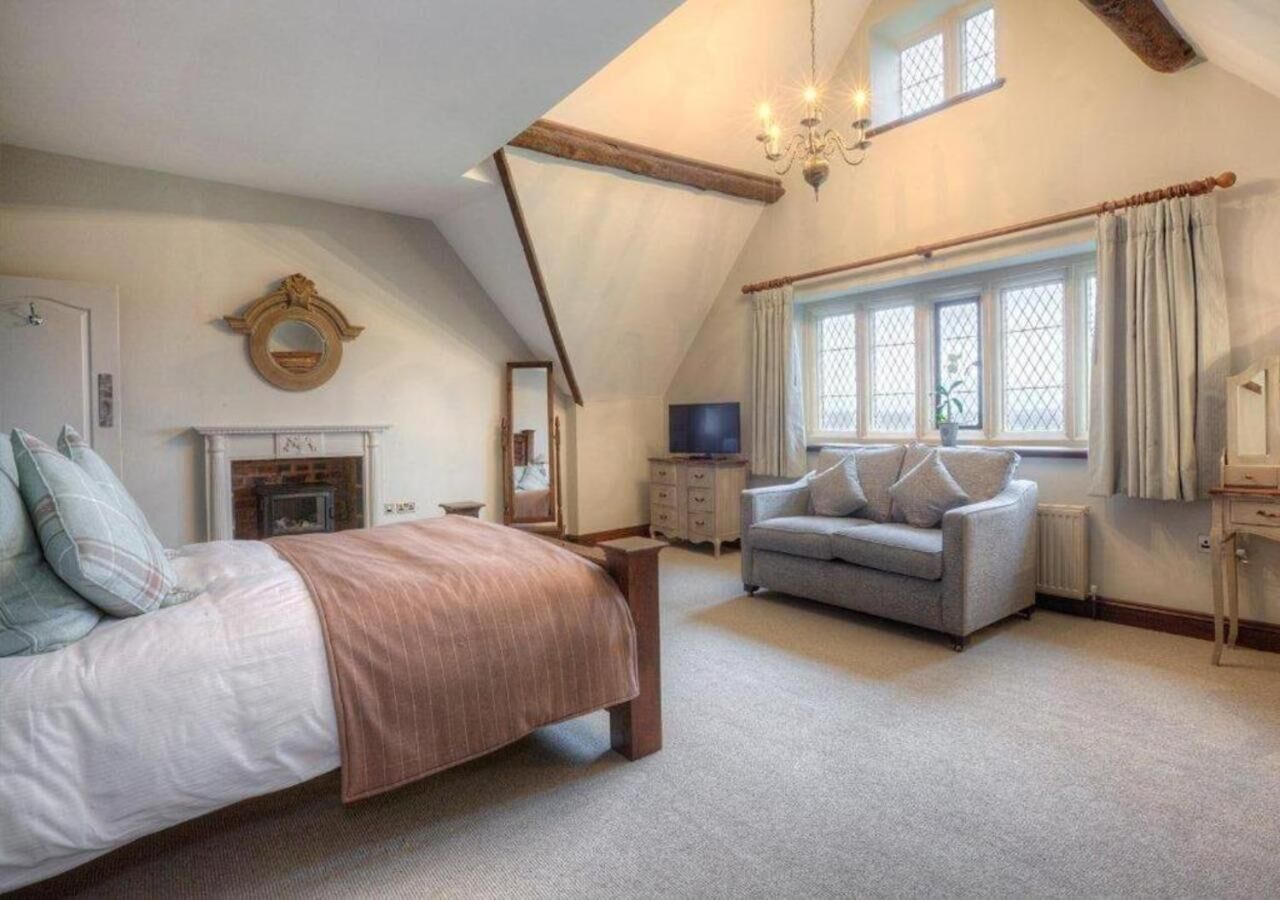 Un dormitorio con cama, sofá, chimenea, televisor y ventana con cortinas.