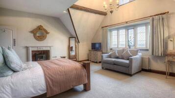 Un dormitorio con cama, sofá, chimenea, televisor y ventana con cortinas.