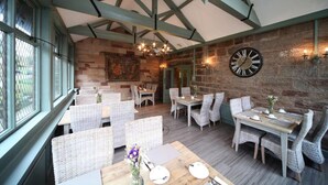 A restaurant with wicker furniture, a wooden ceiling, stone walls, and a large clock. - Weston Hall (Stafford)
