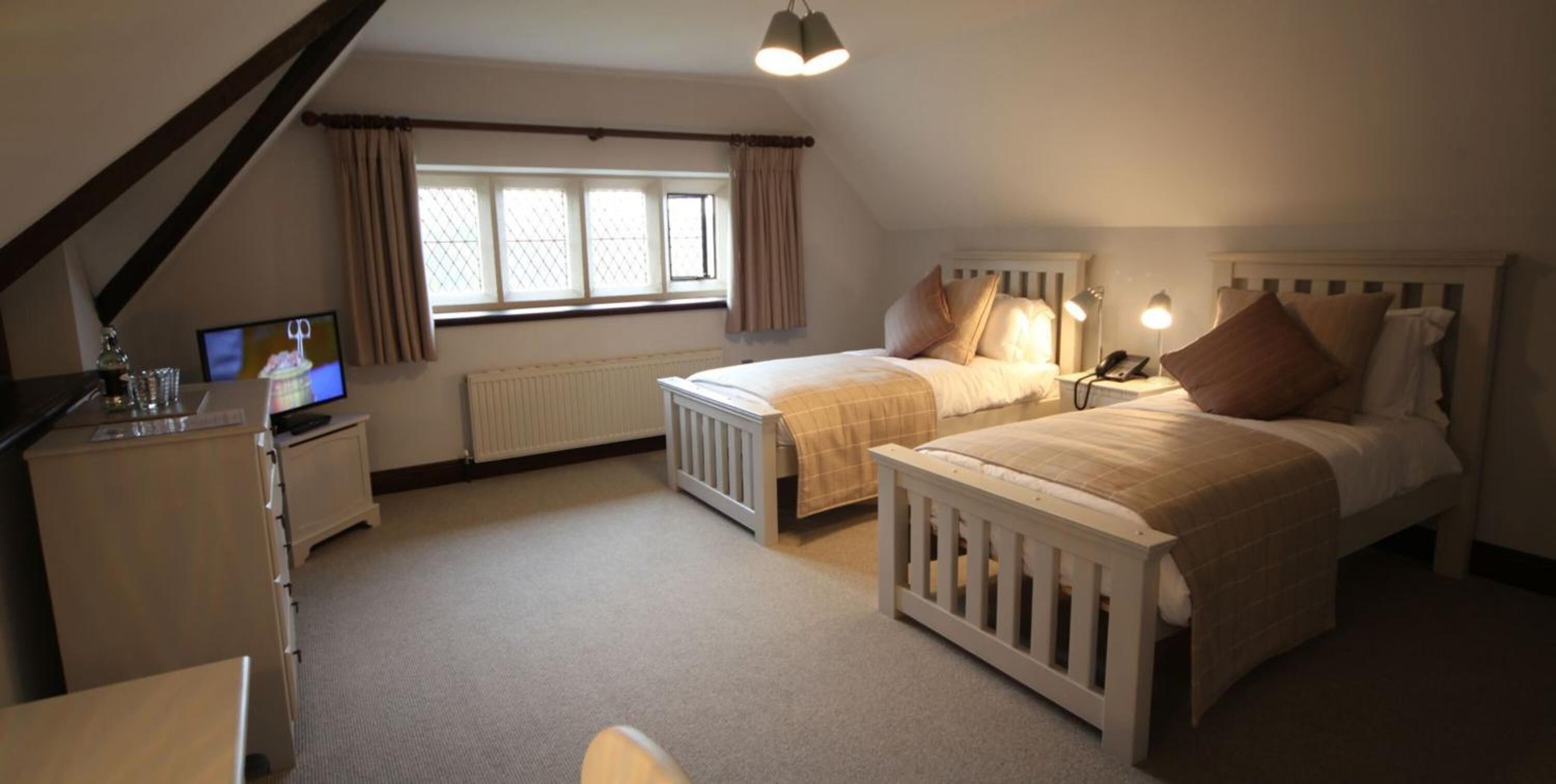 A bedroom with two single beds, a desk with a computer, and a window with curtains.