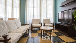 Un salon comprenant un canapé, deux fauteuils, une table basse, un téléviseur et une plante.