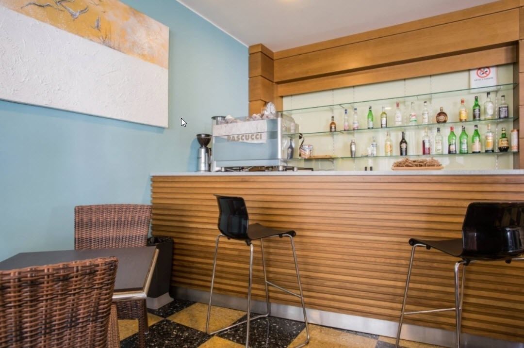 A bar area with a counter, bar stools, a coffee machine, and a shelf with various bottles.
