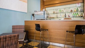 Un espace bar comprenant un comptoir, des tabourets de bar, une machine à café et une étagère où sont rangées diverses bouteilles.
