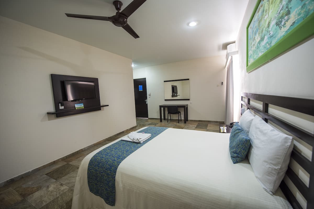 Une chambre d’hôtel équipée d’un lit, d’un téléviseur à écran plat fixé au mur, d’un bureau et d’un ventilateur de plafond.
