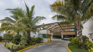 A modern building with a covered entrance, palm trees, and well-maintained landscaping. - Hotel Andiroba Palace (Tuxtla Gutierrez)