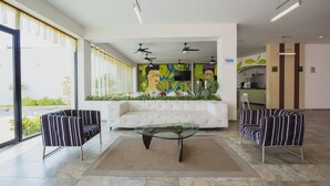 A spacious lobby with a white sofa, striped armchairs, a glass coffee table, ceiling fans, and a large window with a view of greenery. - Hotel Andiroba Palace (Tuxtla Gutierrez)