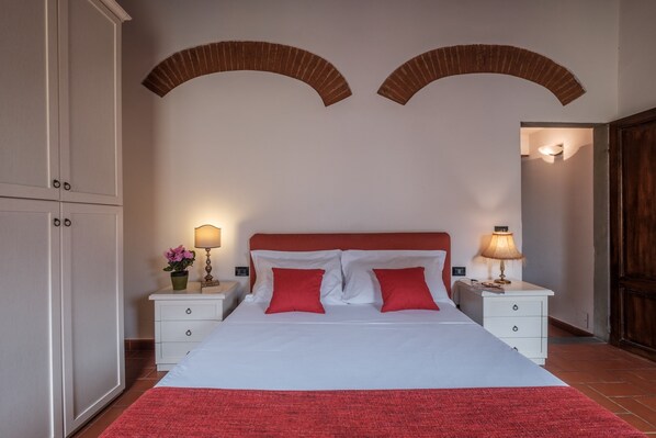 A bedroom with a bed, two nightstands, a wardrobe, and arched brick ceilings.