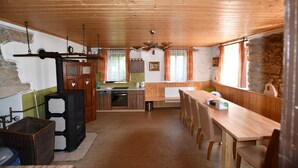 Ett mysigt rum inrett som en stuga, med ett träpanelat tak, en vägg av sten, ett matbord med stolar, en köksdel med en spis och ett fönster med gardiner.